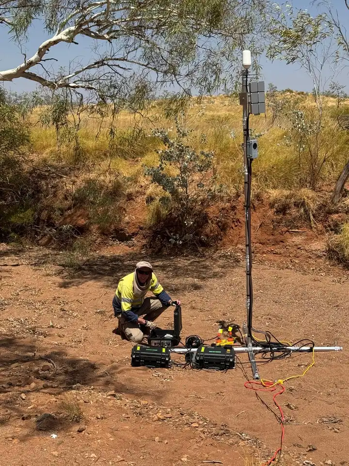 Field engineer setting up an outdoor sensor mast with battery boxes and cabling at an Australian outback site.