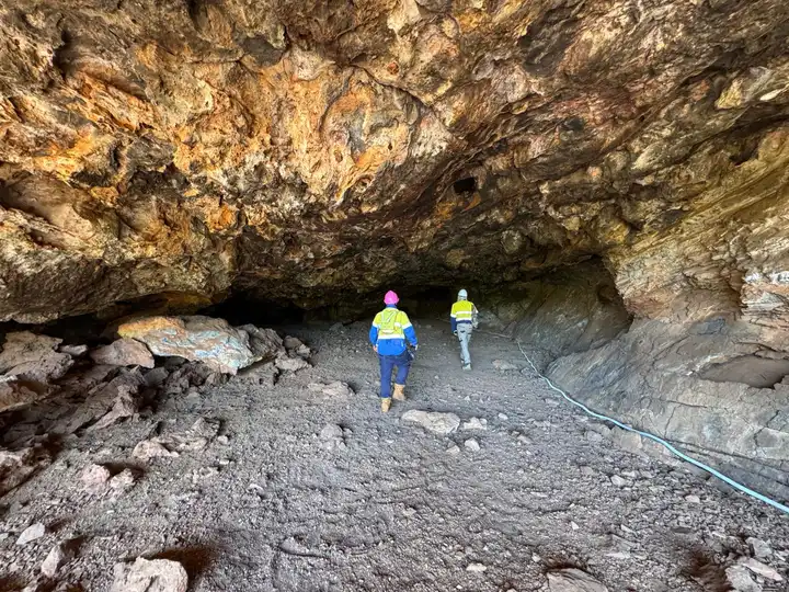 Two field workers in hi-vis walking into a remote cave entrance to install monitoring equipment.