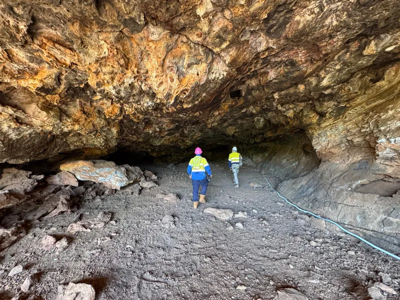 Two field workers in hi-vis walking into a remote cave entrance to install monitoring equipment.